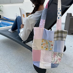 Pode incluir: Uma bolsa tote de patchwork com uma variedade de padrões florais e xadrez em rosa, azul e bege. A bolsa tem duas alças longas e é feita de um tecido de algodão macio.