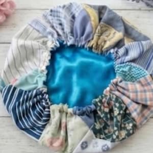 Pode incluir: Um gorro de patchwork com uma variedade de padrões de tecido em tons de azul, branco e amarelo. O interior é de cetim turquesa. O gorro é franzido na borda com uma faixa elástica.