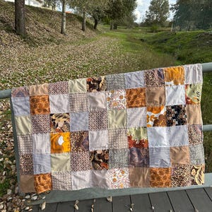 Può includere: Una trapunta patchwork con quadrati di diversi tessuti marroni, beige e bianchi. La trapunta è realizzata con diversi motivi, tra cui floreali, geometrici e con stampa animalier.