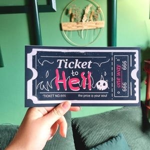Könnte beinhalten: Ein dunkelblaues Ticket mit den Worten "Ticket to Hell" in Rosa und Weiß. Das Ticket hat eine Totenkopf-Grafik und den Text "the price is your soul". Das Ticket wird vor einem grünen Hintergrund gehalten.