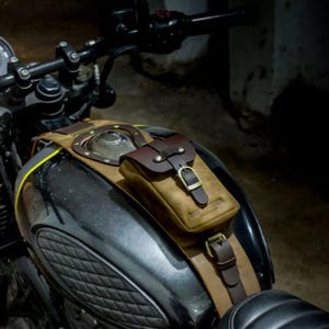 Pode incluir: Um depósito de motocicleta com uma bolsa de depósito de couro castanho e bege. A bolsa tem um pequeno bolso com fecho de fivela. A motocicleta é preta com uma faixa amarela.