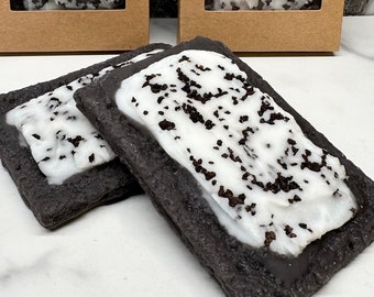 Puede incluir: Dos Pop Tarts de galletas y crema con glaseado blanco y chispas de chocolate. Los Pop Tarts son de color marrón oscuro y de forma rectangular. Dos Pop Tarts están fuera de las cajas y dos están dentro de cajas marrones con una ventana transparente.
