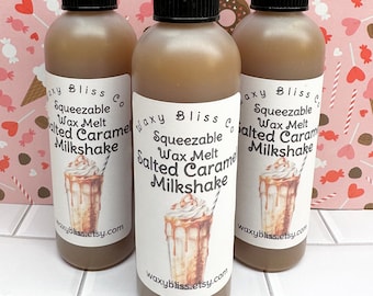 May include: Three brown squeeze bottles with black caps and white labels. The labels read "Squeezable Wax Melt Salted Caramel Milkshake" with an illustration of a milkshake. The background is a pink pattern with hearts and donuts.