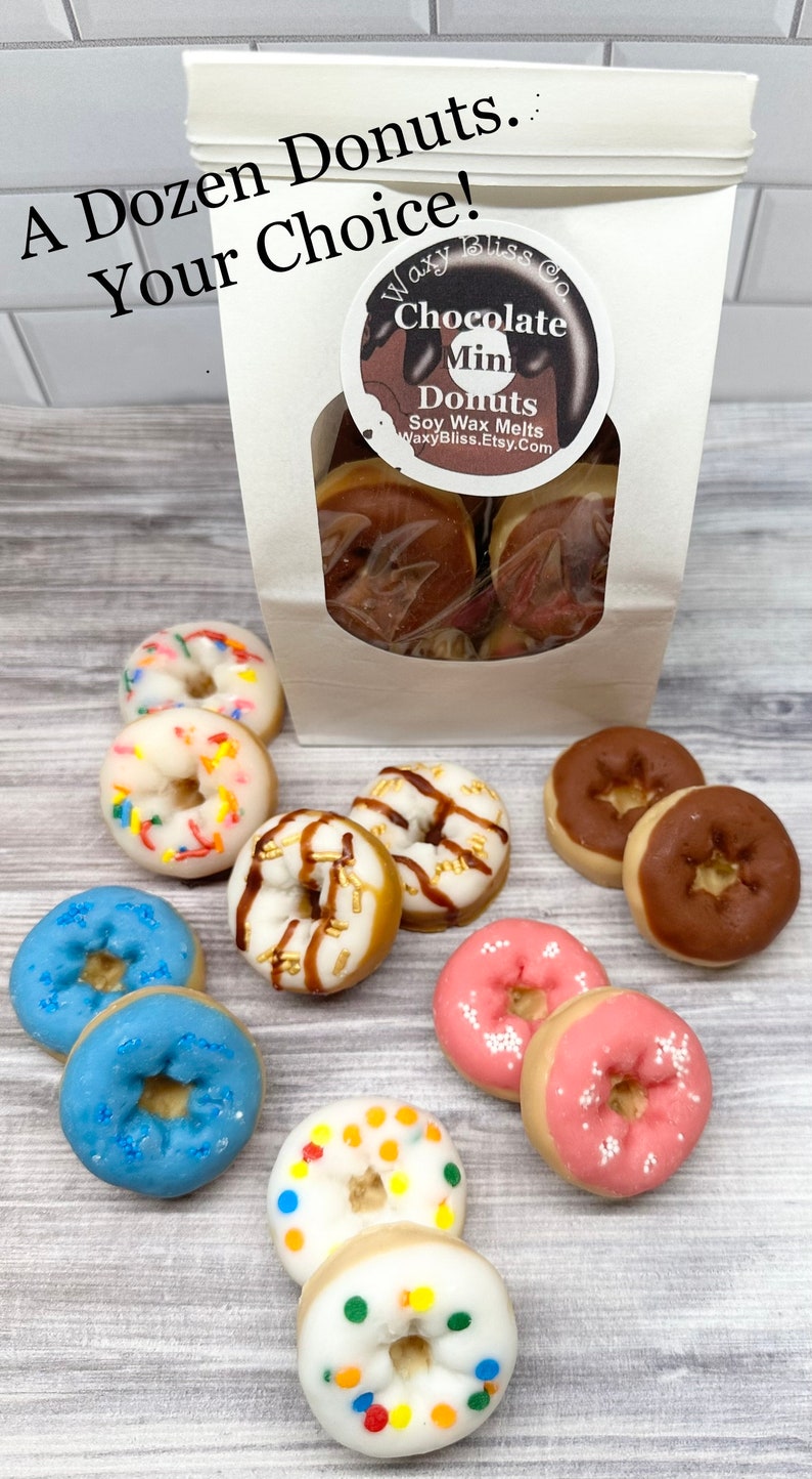 May include: A dozen mini donut-shaped soy wax melts in various colors and toppings, including chocolate, sprinkles, and glaze. The donuts are displayed on a light wood-grain surface, with a bag of donuts in the background.