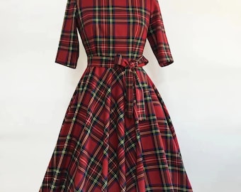 May include: A red plaid dress with a scoop neckline and elbow-length sleeves. The dress features a fitted bodice, a flared skirt, and a matching tie belt. The plaid pattern includes red, green, yellow, and navy blue lines. The dress is displayed on a mannequin.