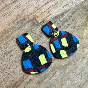 May include: A pair of geometric patterned earrings with a black, blue, yellow, and maroon color scheme. The earrings are made of polymer clay and have a textured finish.