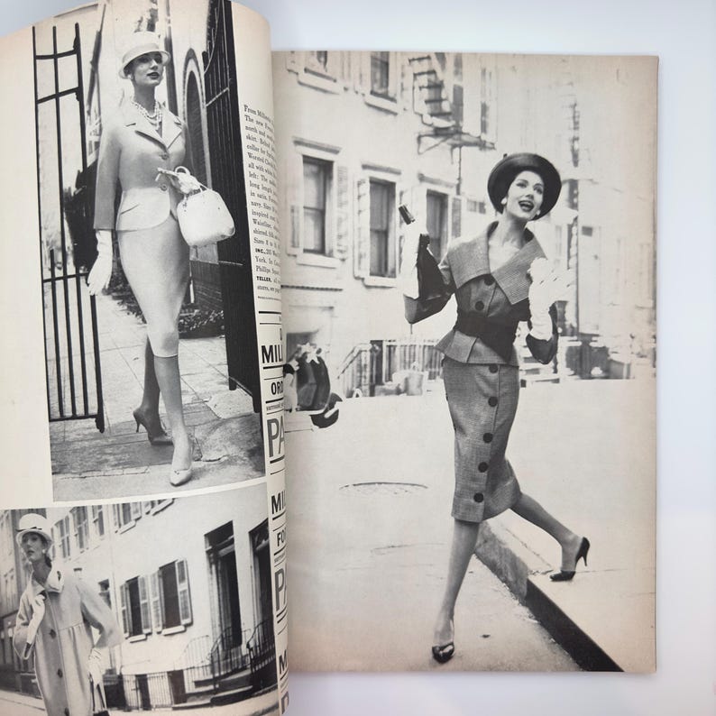 May include: Two women wearing stylish outfits in a black and white photograph. The woman on the left is wearing a white suit with a white hat and a white handbag. The woman on the right is wearing a grey suit with a black hat and a black belt. Both women are walking down a city street.