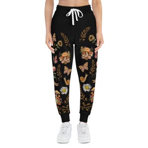 May include: Black sweatpants with a floral print featuring butterflies, mushrooms, and snails. The print is in shades of brown, yellow, and pink.