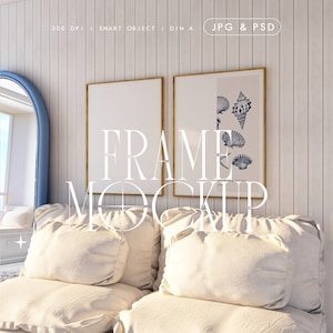 Puede incluir: Dos cuadros enmarcados colgados en una pared de madera blanca sobre un sofá blanco con dos almohadas blancas. La imagen de la izquierda está en blanco y la imagen de la derecha tiene una ilustración azul y blanca de conchas marinas.