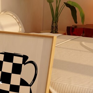 May include: A framed black and white illustration of a vase with a checkered pattern. The frame is made of wood and has a light brown finish. The illustration is on a white background.