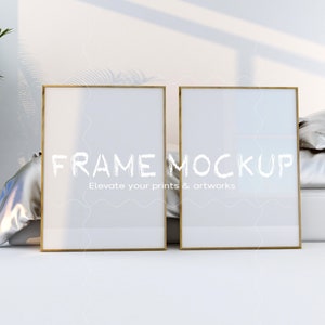 May include: Two gold picture frames with white mats are on a white surface. The frames are empty and ready for your artwork. The text "FRAME MOCKUP" is written in white on the surface. The text "Elevate your prints & artworks" is written below the first text.