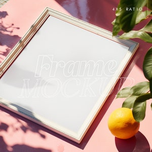 May include: White picture frame mockup on a pink surface with a green plant and an orange. The frame is 4x5 ratio. The text "Frame Mockup" is written in white on the frame.