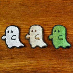 May include: Three embroidered ghost patches in white, beige, and green. The ghosts are all facing the same direction and have a simple, cartoon-like design.