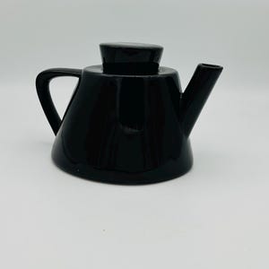 May include: A black teapot with a matching lid and a curved handle. The teapot has a spout for pouring and a rounded body. The design is minimalist and modern, suitable for serving tea.