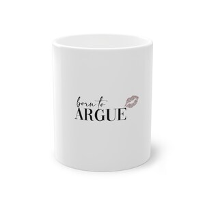 Könnte beinhalten: Weißer Keramikbecher mit dem Schriftzug "born to ARGUE" in schwarzer Schrift, begleitet von einem kleinen, mauvefarbenen Lippenabdruck. Der Becher ist zylindrisch und hat eine glänzende Oberfläche.