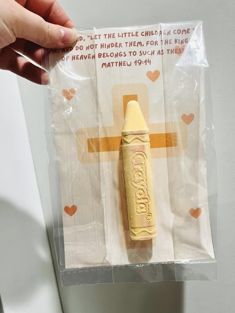 May include: A yellow crayon with the word "Crayola" printed on it, packaged in a clear plastic bag with a white card. The card has a cross and hearts printed on it and the text "Let the little children come to me, and do not hinder them. For the kingdom of heaven belongs to such as these. Matthew 19:14"