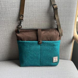 Peut inclure: Un sac bandoulière composé d'une partie supérieure marron foncé et d'une partie inférieure en textile texturé bleu sarcelle. Il est doté d'une sangle en cuir marron avec boucle métallique, d'une patte centrale verticale et d'une étiquette.