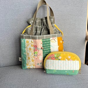 Puede incluir: Una bolsa de mano de patchwork con cierre de cordón y una bolsa más pequeña a juego. La bolsa está hecha de una variedad de telas en tonos de verde, amarillo, rosa y blanco. La bolsa presenta un estampado floral y pájaros.