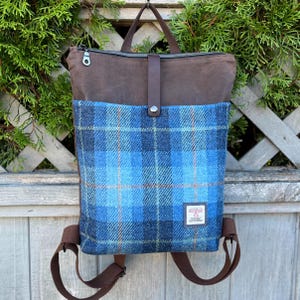 Peut inclure: Un sac à dos en toile cirée marron avec une grande poche avant en laine à carreaux bleus et bleu foncé. Le sac possède une poignée supérieure, des bretelles marron réglables, un compartiment principal zippé et une sangle centrale en cuir.