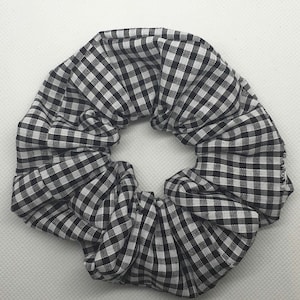 May include: Black and white gingham hair scrunchie. The scrunchie is made of fabric with a checkered pattern.