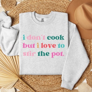 May include: A gray sweatshirt with the text "i don't cook but i love to stir the pot." in colorful letters.