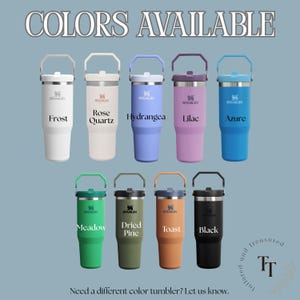 May include: A collection of Stanley tumblers in various colors, including white, pink, blue, purple, green, brown, and black. Each tumbler has a handle and the Stanley logo. Text at the top reads "COLORS AVAILABLE".