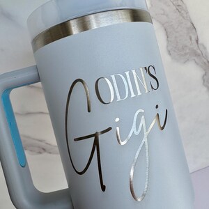 Pode incluir: Um copo t&eacute;rmico azul claro com uma al&ccedil;a e uma borda prateada. O copo apresenta o texto "ODIN'S Gigi" em prata. A tampa &eacute; azul clara com um bot&atilde;o cinza.