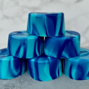 May include: A stack of seven blue and teal swirl soap bars. The bars are arranged in a pyramid shape.