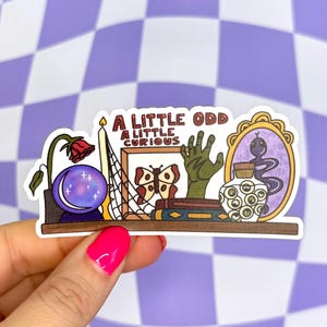 May include: A sticker featuring a shelf with various mystical items. Includes a crystal ball, a rose, a candle, a framed butterfly, a green hand, a mirror with a snake, and a potion bottle. The text reads "A LITTLE ODD A LITTLE CURIOUS."