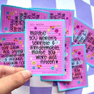May include: Pink stickers with a light blue border and the text "Maybe you weren't terrible & irredeemable, maybe you were just fifteen." The stickers have smiley faces, rainbows, and stars.