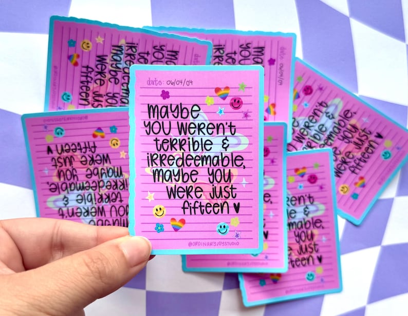 May include: Pink stickers with a light blue border and the text "Maybe you weren't terrible & irredeemable, maybe you were just fifteen." The stickers have smiley faces, rainbows, and stars.