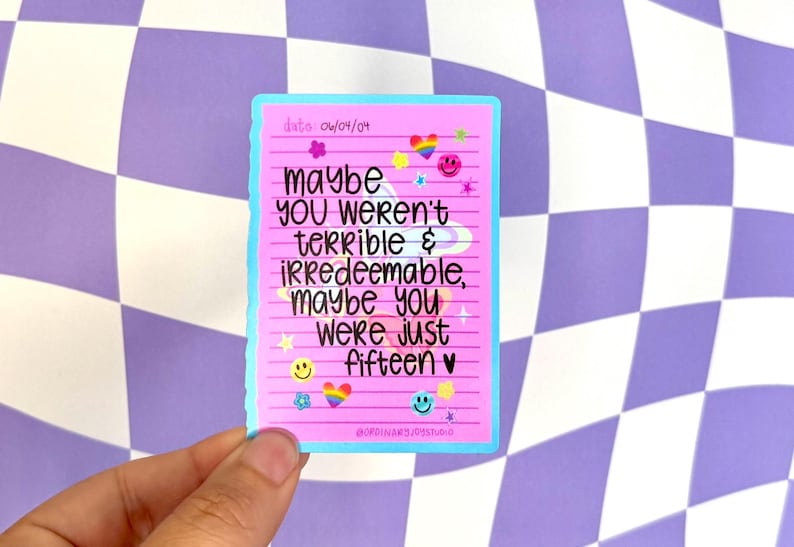 May include: A pink sticker with the text "maybe YOU weren't terrible & irredeemable, maybe you were just fifteen" in black. The sticker has a light blue border and is decorated with smiley faces, hearts, and rainbows.
