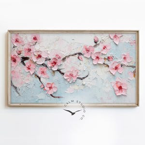 May include: A framed painting of a blossoming cherry tree branch. The artwork features textured, raised pink flowers and dark brown branches against a light blue and white background. The frame is a light wood color.