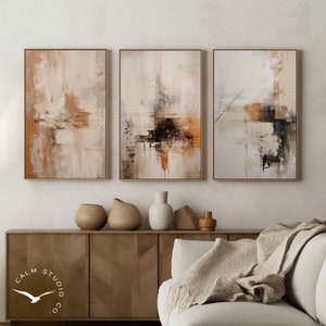 Pode incluir: Conjunto de três impressões de arte abstrata em tons neutros. Cada obra de arte emoldurada apresenta um design texturizado e em camadas com tons bege, castanho e preto. O logotipo Calm Studio Co. é visível no canto inferior esquerdo.
