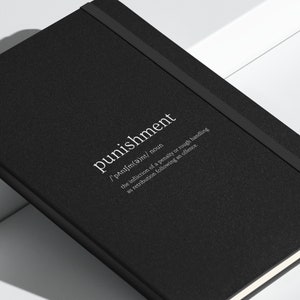 Op de afbeelding: Zwart notitieboek met een witte elastische band sluiting. De voorkant heeft het woord "punishment" in wit gedrukt met een definitie eronder.