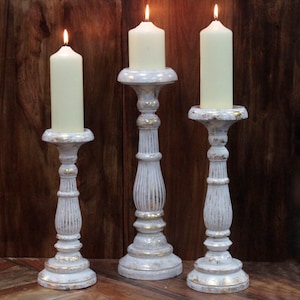 May include: Set of three white wooden candle holders with gold accents. The candle holders are of varying heights and feature a fluted design.