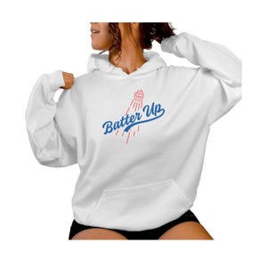 May include: White hoodie with a blue and red graphic of a cupcake flying through the air with the text "Batter Up" in a vintage baseball font.