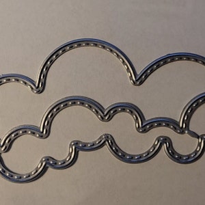May include: A die-cut metal cloud shape with a series of small, evenly spaced holes along the edges. The cloud is silver in color and has a three-dimensional appearance, suggesting it may be used for crafting or scrapbooking projects.