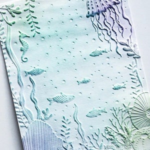 May include: An embossed art print featuring an underwater scene. The design includes a jellyfish, seahorse, fish, and various aquatic plants. The color palette transitions from light blue to green, with touches of purple.