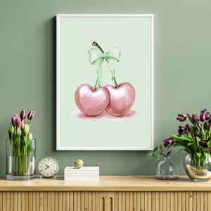May include: A watercolor painting of two pink cherries with green stems and a green bow tied around the stems. The cherries are on a light green background.