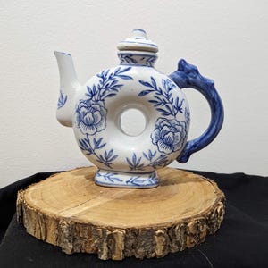 May include: A white ceramic teapot with a blue and white floral design. The teapot has a round body with a hole in the center and a dragon-shaped handle.