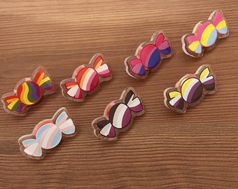 Puede incluir: Siete pines con forma de caramelo de colores con diferentes diseños de banderas del orgullo. Los pines están hechos de plástico transparente con un diseño colorido en el interior. Los diseños incluyen las banderas del orgullo bisexual, lesbiana, transgénero, pansexual, genderfluid y asexual.