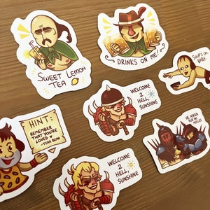 May include: A set of nine stickers featuring various cartoon characters and text. The stickers are printed on white paper with a glossy finish. The characters include a man with a moustache drinking tea, a man with a hat holding two mugs of beer, a man with a helmet and a sword, a man with a helmet and a sword, a man with a helmet and a sword, a man with a helmet and a sword, a man with a helmet and a sword, a man with a helmet and a sword, and a man with a helmet and a sword. The text on the stickers includes "Sweet Lemon Tea", "Drinks on Me", "Welcome 2 Hell, Sunshine", "Hint: Remember that you're loved -Terr Bear", "He Asked for No Pickles", and "Soup's On, Baby."