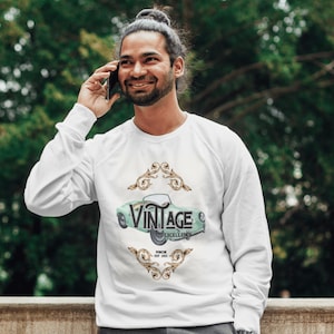 May include: White sweatshirt featuring a vintage car design in light green with the word "VINTAGE" above it. The design includes the words "EXCELLENCE" and "PORSCHE EST 2021". The sweatshirt is worn by a person.