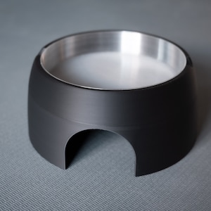 May include: A black elevated pet bowl with a stainless steel interior. The bowl has a raised lip and a cutout on the bottom for easy cleaning.