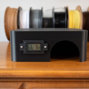 K&ouml;nnte beinhalten: Schwarzes 3D-gedrucktes Geh&auml;use mit einem digitalen Display, das 51 % und 76 Grad anzeigt. Das Geh&auml;use hat eine kleine &Ouml;ffnung an der Vorderseite.