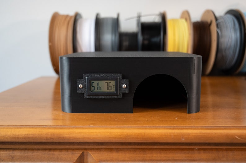 K&ouml;nnte beinhalten: Schwarzes 3D-gedrucktes Geh&auml;use mit einem digitalen Display, das 51 % und 76 Grad anzeigt. Das Geh&auml;use hat eine kleine &Ouml;ffnung an der Vorderseite.