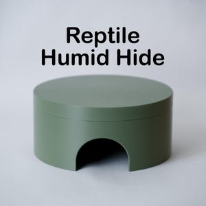 May include: A sage green reptile humid hide with a rounded top and a semi-circular opening. The text "Reptile Humid Hide" is printed in black above the hide.