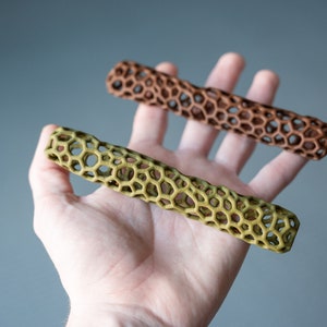 May include: Two 3D printed, hollow, cylindrical objects with a honeycomb pattern. One is brown and the other is green.