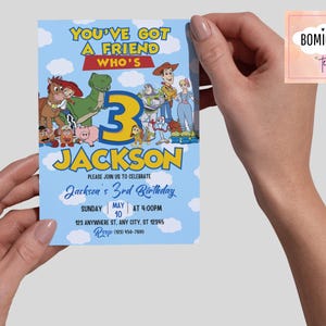 K&ouml;nnte beinhalten: Eine hellblaue Geburtstagseinladung mit Charakteren aus Toy Story. Die Einladung lautet "You've Got a Friend Who's 3 Jackson" mit Veranstaltungsdetails. Die Einladung wird von einer Person gehalten.